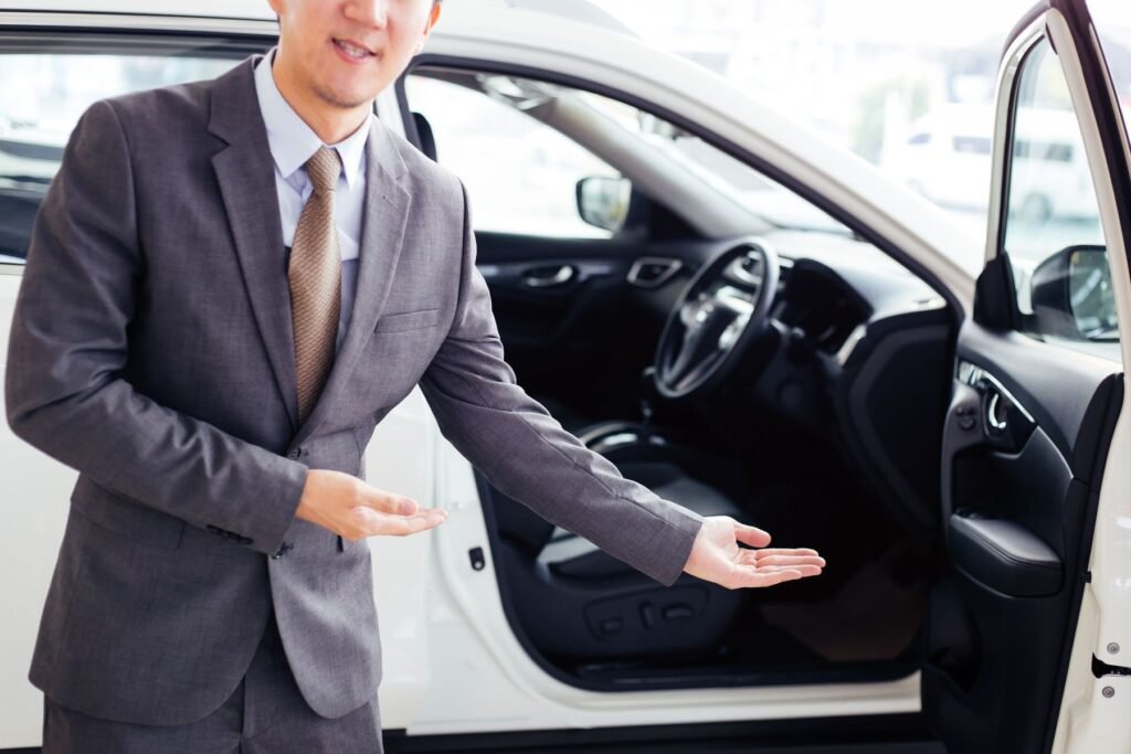 Chauffeur in a suit gesturing toward an open car door