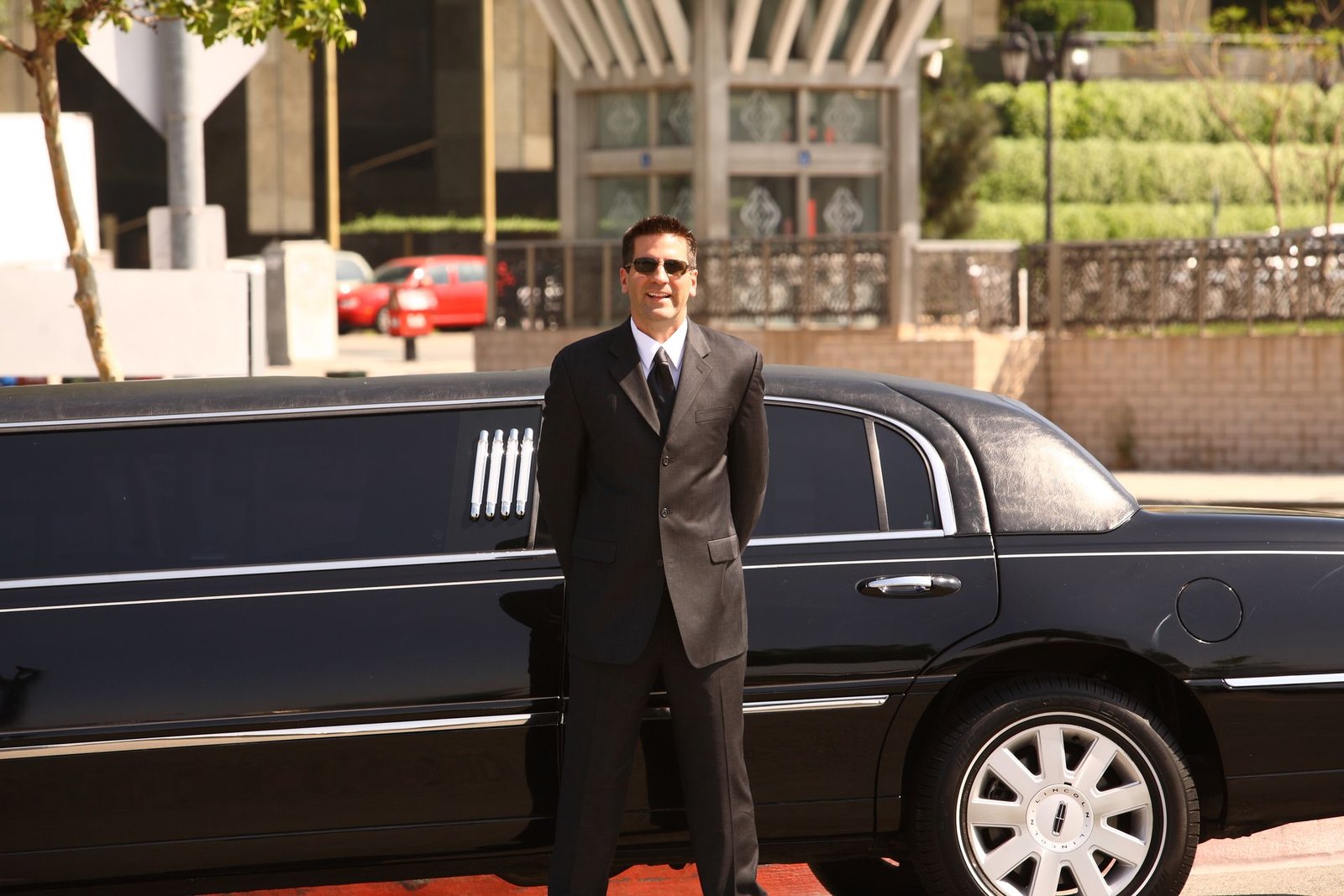 Chauffeur in suit and sunglasses standing by a black Lincoln limousine