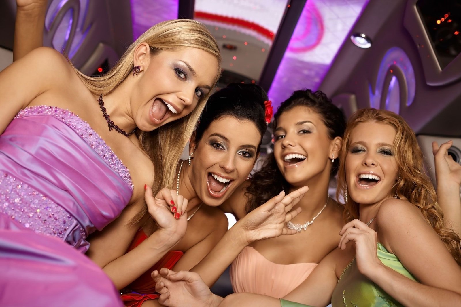 Four people in formal dresses laughing inside a limousine with purple lighting